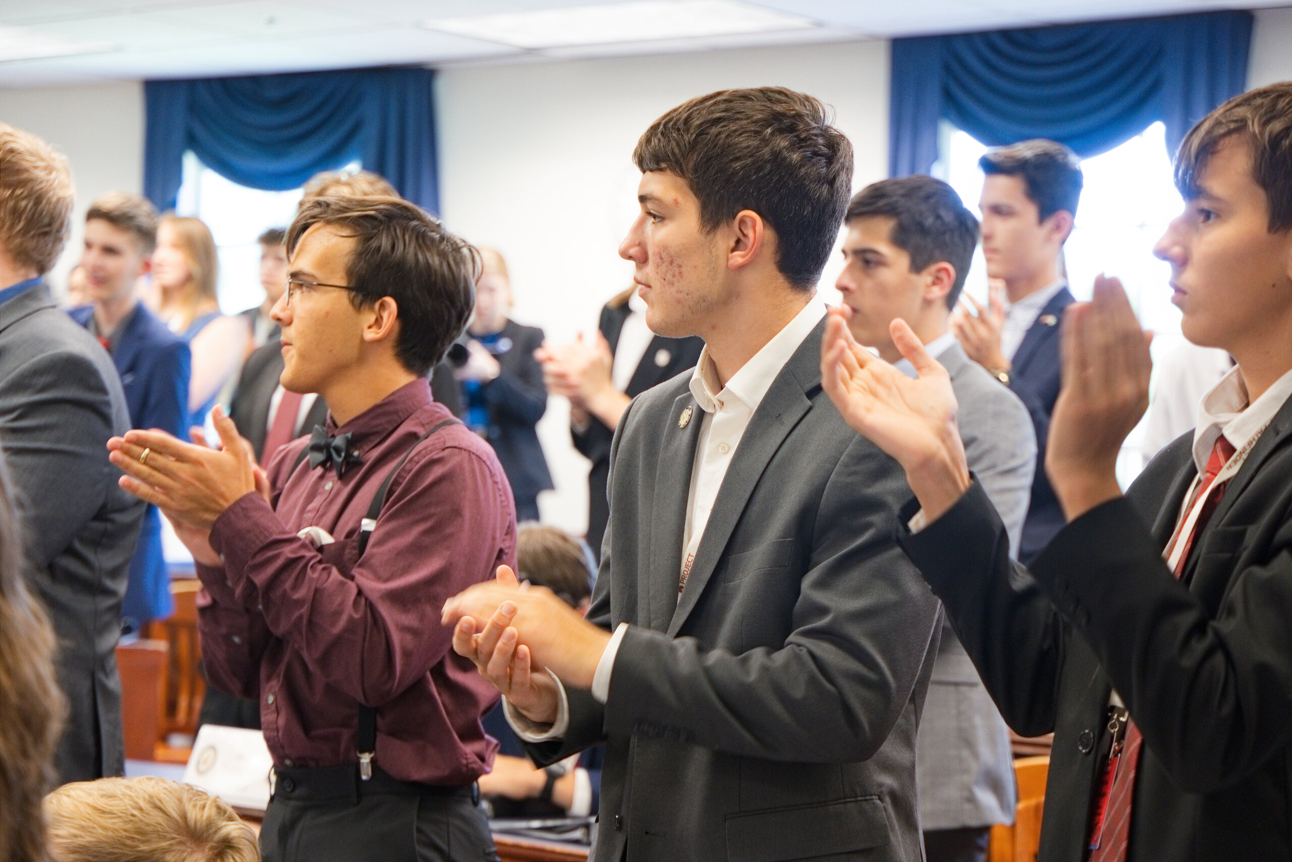 Students in blazers and bow ties stand applauding during a mock Senate session