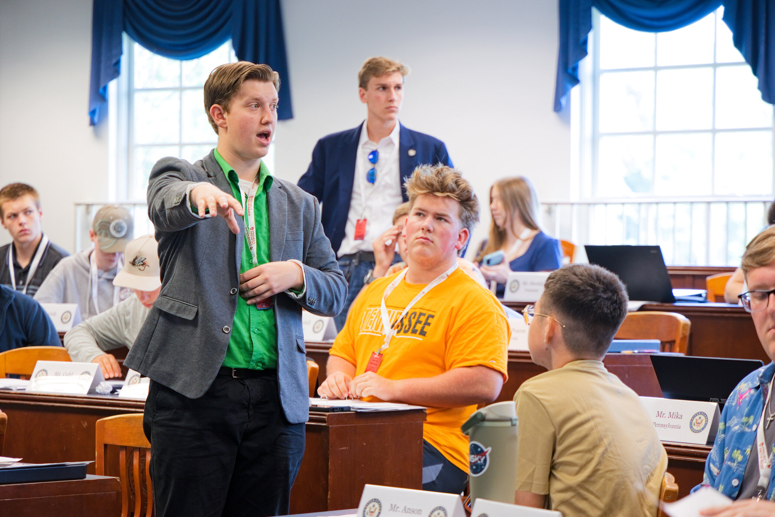 Student in a green shirt and gray blazer gestures while debating in a mock Senate session