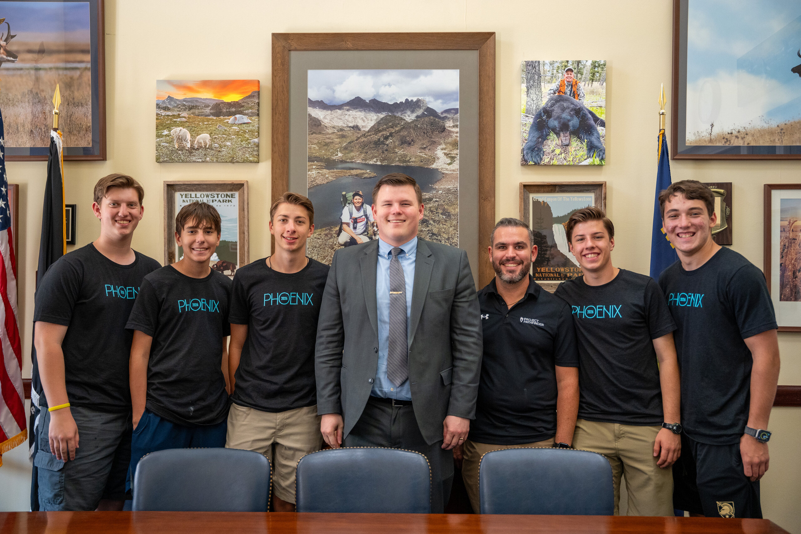 Campers and leaders pose with a suited staffer in an office decorated with wildlife photos